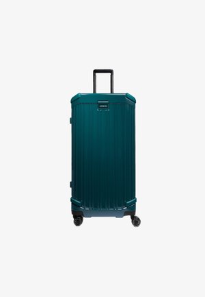 Maleta de concha dura color azul verdoso con ranuras verticales, asa retráctil y cuatro ruedas negras. Cuenta con una placa con el logo en la parte frontal.