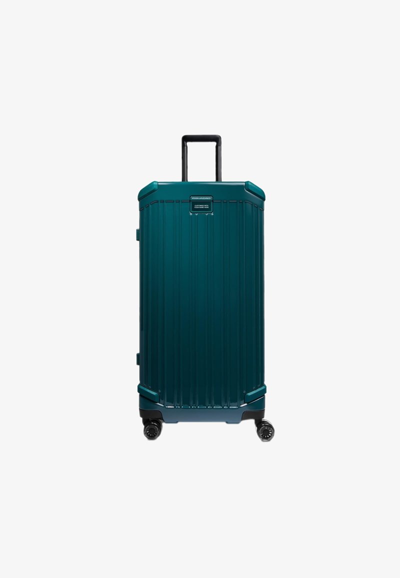 Tegelkleurige harde koffer met verticale groeven, een uitschuifbaar handvat en vier zwarte wielen. Voorzien van een logoplaatje aan de voorzijde.