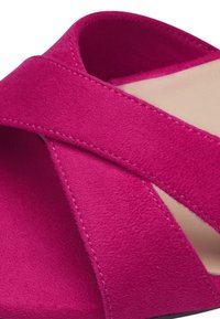 Gros plan d'une sandale en daim rose à bout ouvert avec des brides croisées et une doublure intérieure beige.