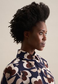Blusa con colletto caratterizzata da uno sfondo blu navy con grandi motivi floreali crema e marroni. Tessuto liscio con una vestibilità strutturata e bottoni.