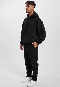 Felpa nera con cappuccio e pantaloni in morbido misto cotone, con tasca frontale e logo discreto. Abbinati a sneakers bianche.