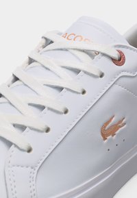 Λευκό δερμάτινο αθλητικό παπούτσι με λευκά κορδόνια, ροζ χρυσά γαντζάκια και λογότυπο κροκοδείλου στο πλάι.