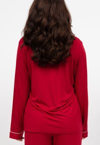 Top de manga larga rojo con un corte holgado y acentos de puños blancos, hecho de una tela suave. La parte trasera cuenta con un material suavemente drapeado.