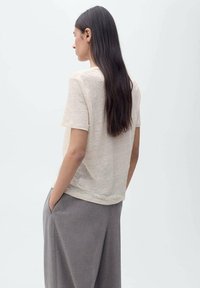 T-shirt beige clair à manches courtes avec une coupe décontractée, fabriqué en tissu doux et texturé. Porté avec un pantalon gris et rentré.