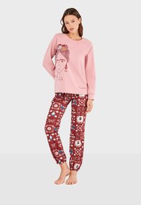 Sweatshirt rose avec un design de visage graphique, associé à un pantalon bordeaux à motifs avec des fleurs et des papillons. Tissus doux, coupe décontractée.