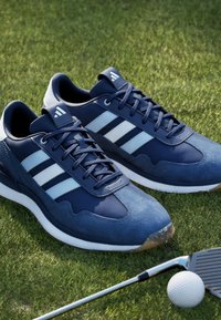Scarpe da ginnastica blu navy con strisce bianche, in camoscio e materiale sintetico, punta arrotondata e suole testurizzate, esposte sull'erba.