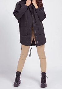 Lekka czarna kurtka z kapturem, zamkiem z przodu i dwoma naszywanymi kieszeniami. Połączona z khaki spodniami o zwężanych nogawkach i czarnymi sznurowanymi butami.