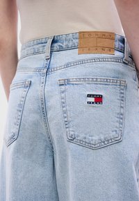 Ανοιχτό μπλε τζιν παντελόνια με κλασική κοπή και δύο πίσω τσέπες. Η ζώνη έχει καστανή δερμάτινη ετικέτα με ανάγλυφο το λογότυπο "TOMMY JEANS".