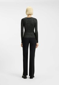 Top nero a maniche lunghe con una lucentezza metallizzata e texture. Design aderente con scollatura a girocollo, abbinato a pantaloni neri sartoriali e stivali neri flat.