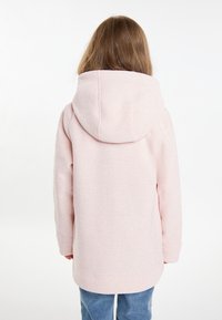 Felpa cappuccio rosa chiaro con una finitura testurizzata, maniche lunghe e vestibilità ampia, abbinata a jeans blu. Design complessivo casual.
