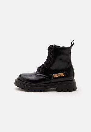 Czarny błyszczący skórzany botek typu combat ze sznurowaniem, grubą podeszwą i złotym logo "Moschino" z boku.