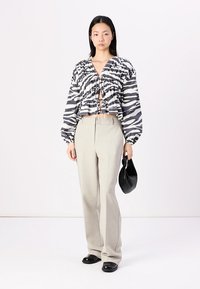 Blusa curta com padrão de zebra em preto e branco, com mangas bufantes, combinada com calças bejes claras e uma pequena mala preta.
