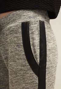 Grå teksturerede joggingbukser med sorte faux læder sidepaneler. Stoffet har et spraglet mønster og har lommer i siderne.
