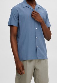 Kortärmad skjorta med knappar i ljusblått tyg, med avslappnad krage, mjuk textur och knappstängning fram.
