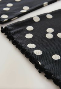 Tissu noir à pois blancs, présentant une texture côtelée et un bord à volants. Vue en gros plan de deux morceaux de tissu.