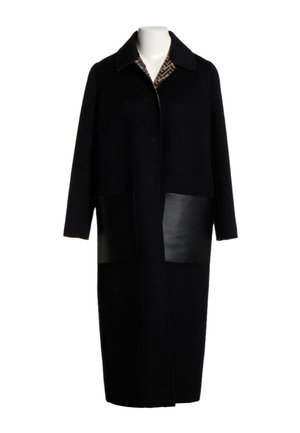Long manteau noir avec un large col, deux grandes poches avant en cuir et une doublure intérieure à motifs visible au niveau de l'encolure.