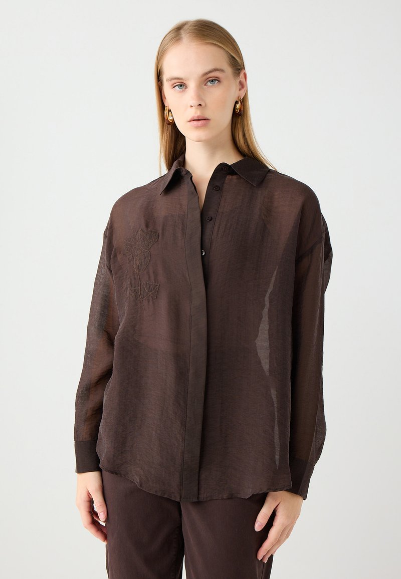 Camicia button-up trasparente marrone con colletto, caratterizzata da un ricamo floreale sul lato sinistro e maniche lunghe e ampie.