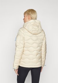 Pufferjack, crème kleur, gequilt golfpatroon, met capuchon, elastische manchetten, zijzak, lichtgewicht materiaal, zachte textuur.