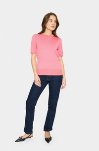 Rosa Kurzarmpullover in Rippstruktur, kombiniert mit dunkelblauen geraden Jeans und schwarzen spitz zulaufenden Schuhen.