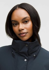 Giacca alta blu scuro con superficie testurizzata. Caratterizzata da bottoni a pressione e un design elegante, adatta per un abbigliamento casual.