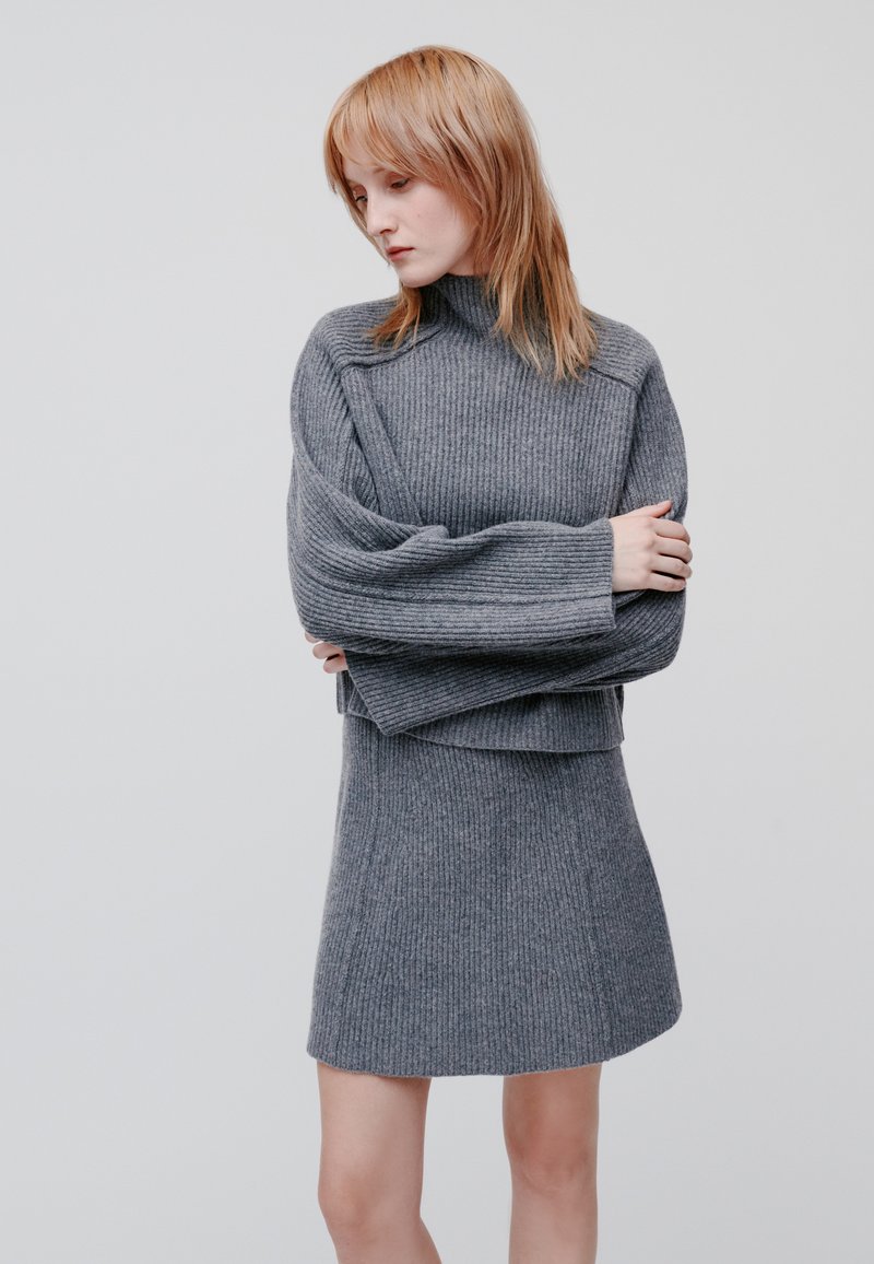 Grauer ribbed Strickpullover mit hohem Kragen und langen Ärmeln, kombiniert mit einem passenden gerippten Rock. Weiche Textur und taillierte Passform.