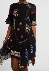 Musta sifonkimekko, jossa on kukkaistikkaus punaisessa, beessissä, sinisessä ja valkoisessa, liehuva helma ja lyhyet hihat, joissa on pitsireunus.