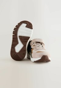 Beige and brown sneakers with a textured suede upper, patterned rubber sole, and contrasting navy and tan accents. Features laces and a strap.