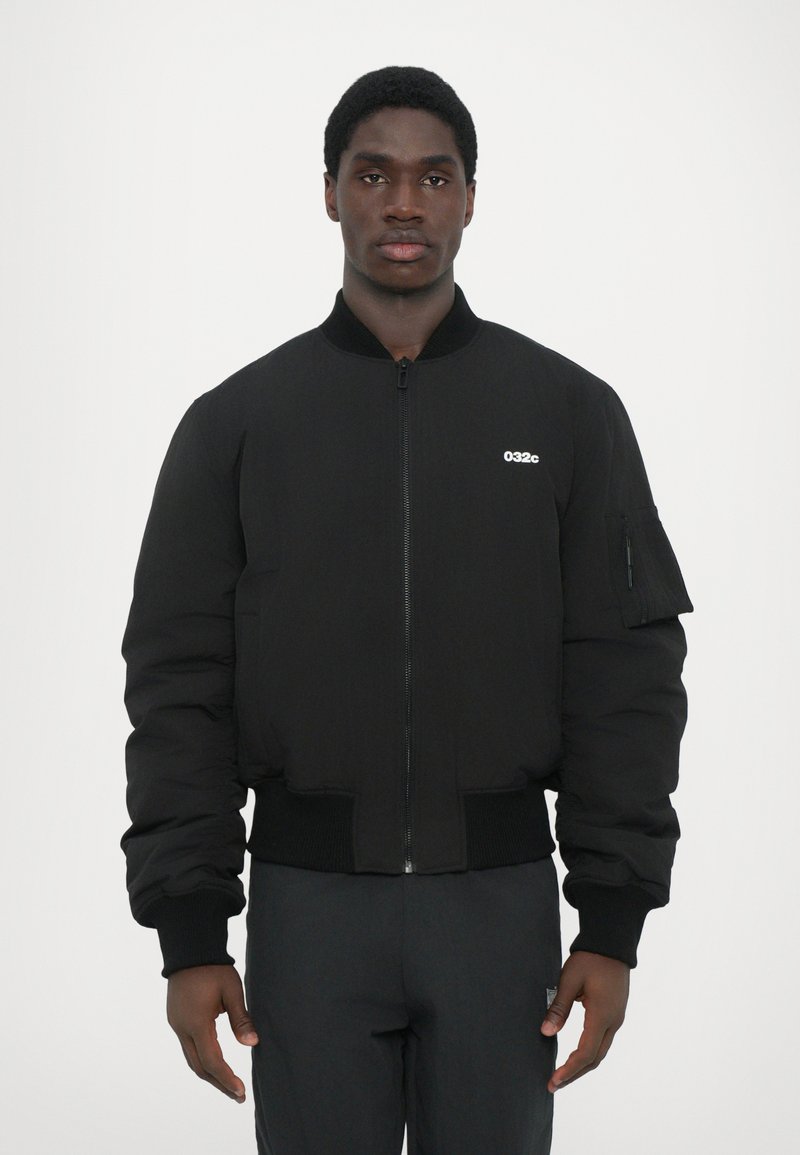 Chaqueta bomber negra de material acolchado con puños y dobladillo acanalados, con cierre de cremallera y un bolsillo en la manga izquierda. Logo de la marca en el pecho.