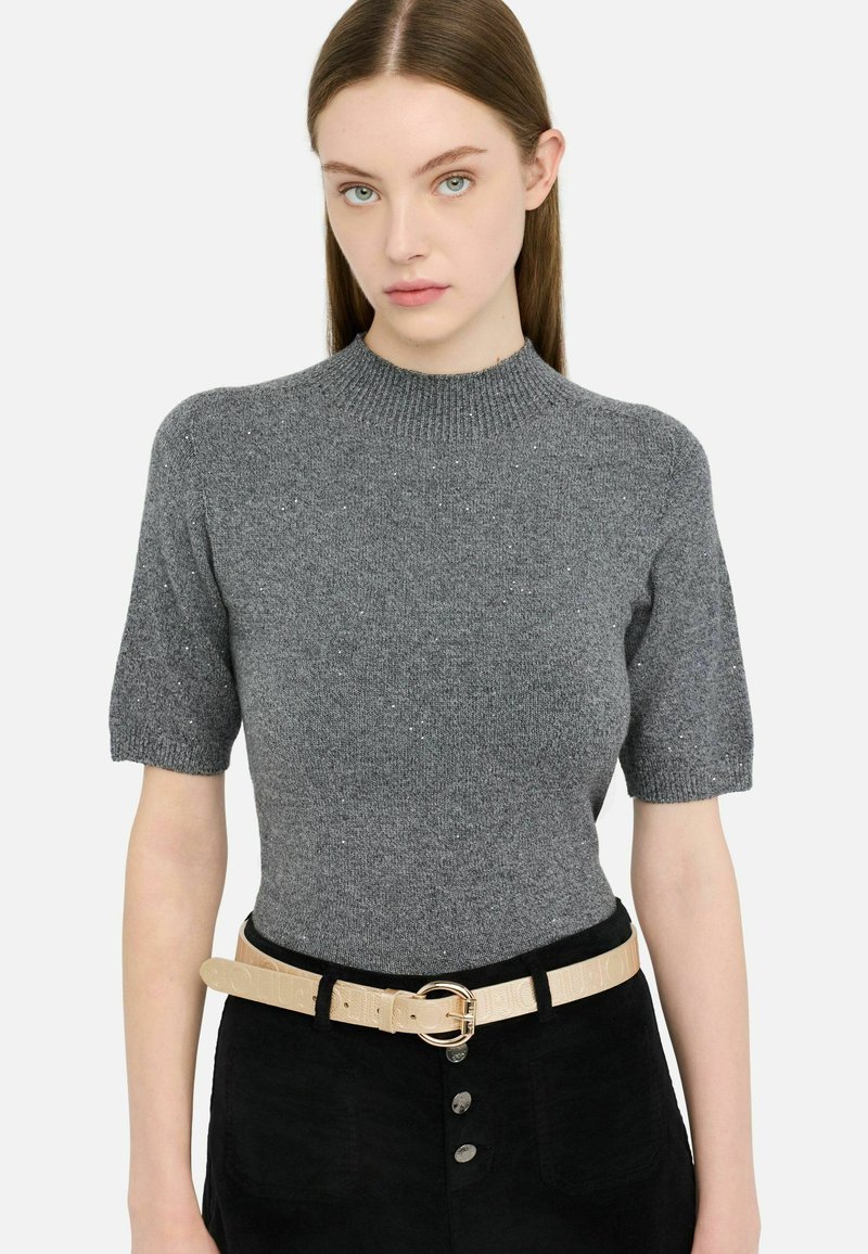 Szary sweter z krótkim rękawem o teksturowanym wykończeniu i delikatnym połysku; w połączeniu z jasnym paskiem z okrągłą klamrą oraz spodniami.
