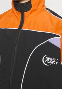 Black and orange windbreaker jacket with white and purple accents, featuring a high collar and full zipper. "NIGHT ADDICT" logo displayed.