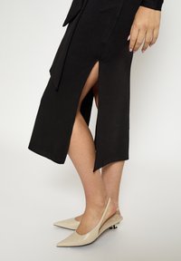 Mustast põlveni ulatuv kleit, millel on kõrged küljeslõiked ja mugav lõige, paaritatud beežide, terava ninaga seljaga kontsakingadega, millel on väike konts.