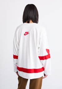 Hvid mesh langærmet trøje med rød Nike-logo, røde horisontale striber og hjerte-mønster på ærmet.