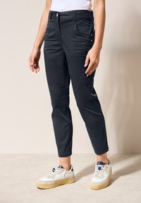 Tmavě modré bavlněné kalhoty slim fit s předními kapsami a dekoračním prošíváním. V kombinaci s bílými teniskami.