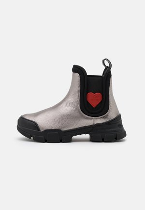 Bottine argentée métallique avec côtés élastiques noirs, semelle noire épaisse et détail cœur rouge avec l’inscription « Love Moschino » sur le côté.