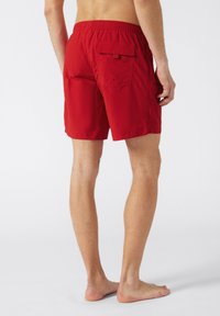 Shorts de bain rouges avec une taille élastique, une poche arrière et un minimum de détails. Fabriqués à partir d'un tissu léger et à séchage rapide.