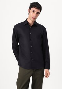 Black long-sleeve shirt with a collared neckline, front button closure, smooth texture, and a straight hem, paired with khaki pants.