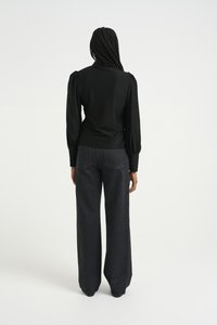 Svart langermet topp med puffermer, kombinert med høyt liv og vide, mørke denimjeans med kontraststing og lommer.