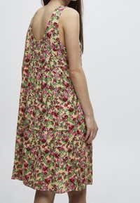 Vestido floral con un diseño sin mangas, patrones coloridos de rosas y tonos verdes sobre un fondo claro, con una falda suelta y un escote bajo.