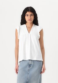 Top bianco a maniche corte con scollatura a V, realizzato in tessuto ad occhiello e con delicati volant sulle spalle. Abbinato a una gonna di jeans.