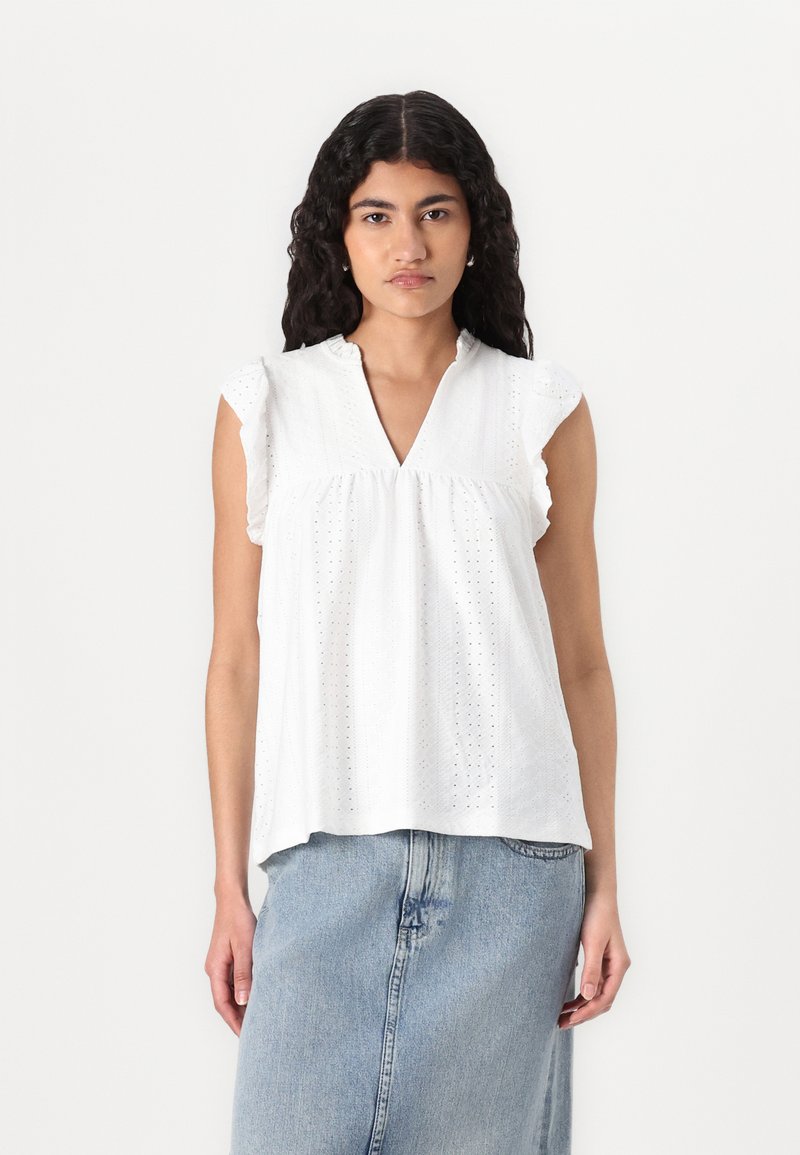 Top bianco a maniche corte con scollatura a V, realizzato in tessuto ad occhiello e con delicati volant sulle spalle. Abbinato a una gonna di jeans.