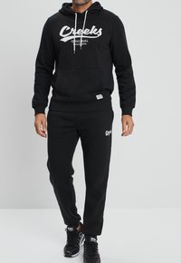 Zwart hoodie en sweatpants set, met een voorzak, trekkoordkap en witte logo-accenten. Gladde stof met een ontspannen pasvorm.