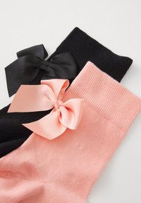 Due paia di calze fino al ginocchio: una nera con un fiocco in raso nero, l'altra rosa con un fiocco a righe rosa chiaro, entrambe caratterizzate da una texture a costine.