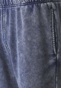 Joggers en denim bleu profond avec une texture délavée. Dotés d'une taille élastique et de poches latérales, ils présentent un design décontracté.