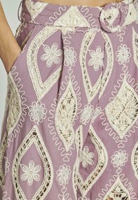 Gonna di tessuto viola con dettagli intricati in pizzo bianco caratterizzati da motivi floreali e vita con cintura. Include tasche laterali.