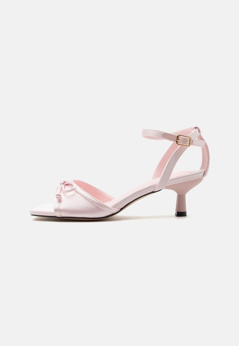 Sandale rose clair à bout ouvert avec un talon kitten, bride à la cheville avec boucle et petit nœud décoratif sur la bride avant.