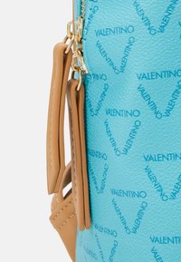 Blå strukturerad läderhandväska med guldiga detaljer och ljusbruna accenter. Har ett mönster med upprepande "Valentino"-logotyp. Dragkedjestängning.