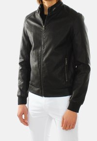 Giubbotto bomber in pelle nera con chiusura a zip, polsini a costine e tasche laterali. Texture liscia e design aderente con colletto alto.
