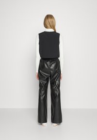 Czarny bezrękawnik na białym golfie, zestawiony z czarnymi, wysokim stanem spodniami z ekologicznej skóry. Gładka faktura i luźny krój spodni.