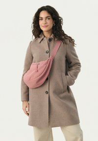Cappotto di lana marrone con colletto e bottoni, abbinato a una grande borsa a tracolla in tessuto rosa con zip e tracolla regolabile.