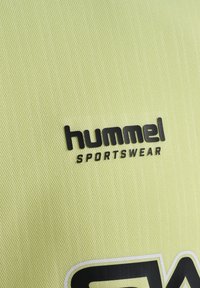 Gul sportstøjsstof med et struktureret mønster. Har et sort "hummel" logo og "SPORTSWEAR" tekst i fed skrift nedenunder.